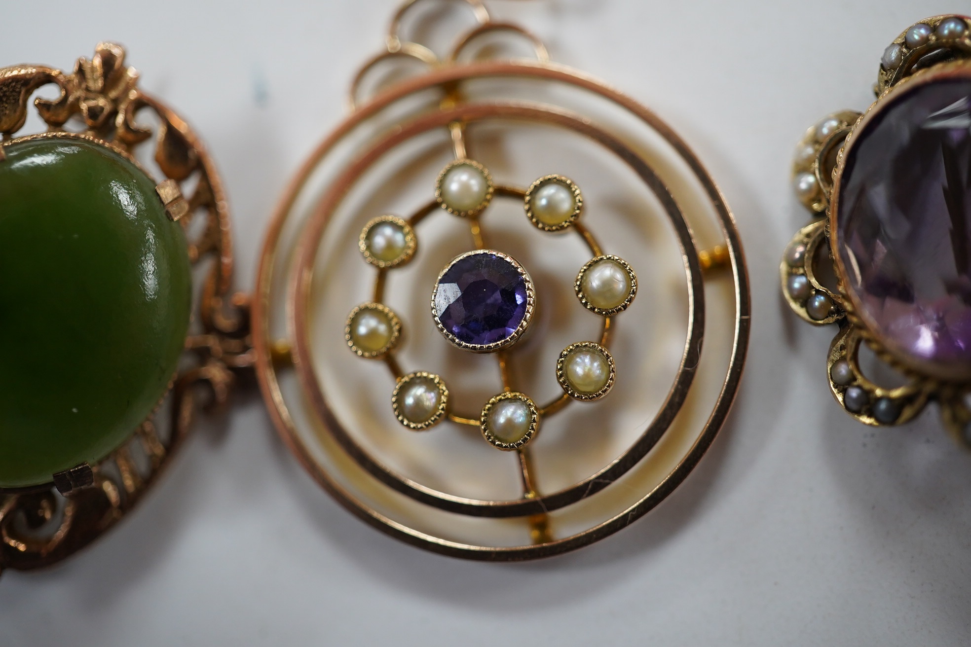 An Edwardian 9ct, sapphire and seed pearl cluster set open work circular pendant, 26mm, together with a similar 9ct, amethyst and seed pearl set brooch and a 9ct and nephrite set brooch, gross weight 7.4 grams. Condition